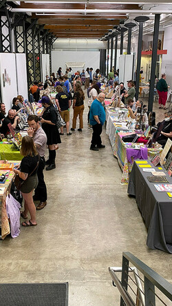 Image of people in the Atrium Gallery of the School of Art and Visual Studies building, looking at tables with art