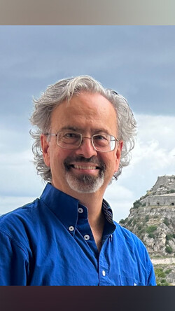 Headshot of Dr. Ben Arnold, wearing a blue button down and glasses against a blue sky 
