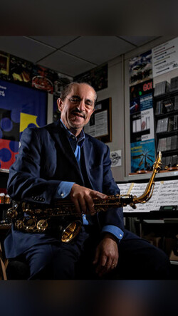 Image of Miles Osland seated, in his studio, holding saxophone.
