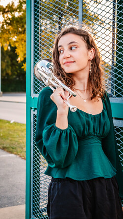Image of Adrianna Dick wearing a teal shirt and black pants, outdoors with her trumpet