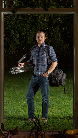 Self portrait photograph of Rob Southard holding photography equipment, in backyard, looking through picture window, 