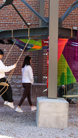 people swinging and colored fabric draped around urban landscape