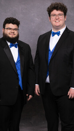 Members of FreshF stand against a grey background wearing tuxedos with blue bowties and vests 