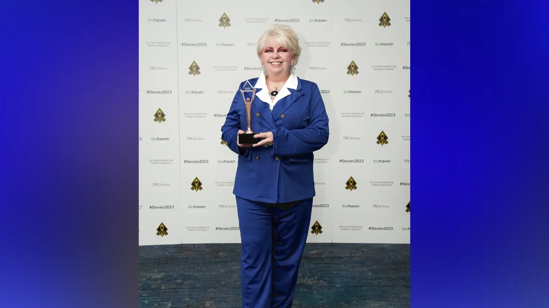 Image of Renee Cobb wearing a blue suit in front of a step and repeat holding her award