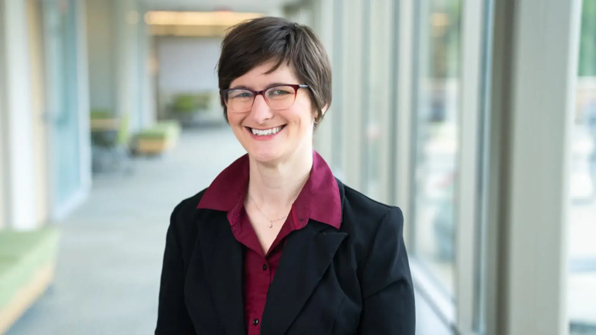 Abigail Van Klompenberg in a black blazer and red shirt, wearing glasses.