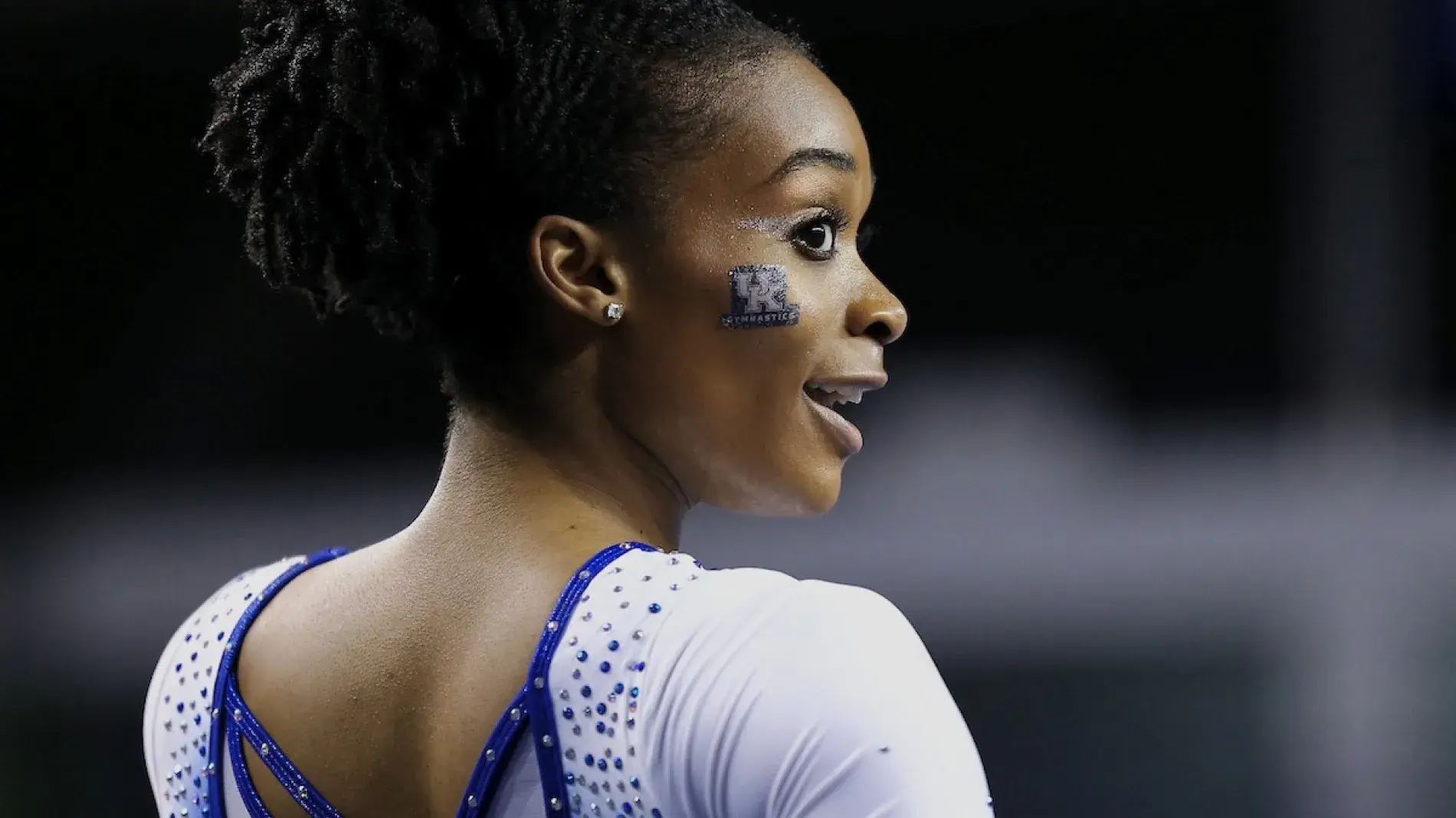 Image of UK student athlete in gymnastics leotard and the UK lockup in facepaint on her cheek