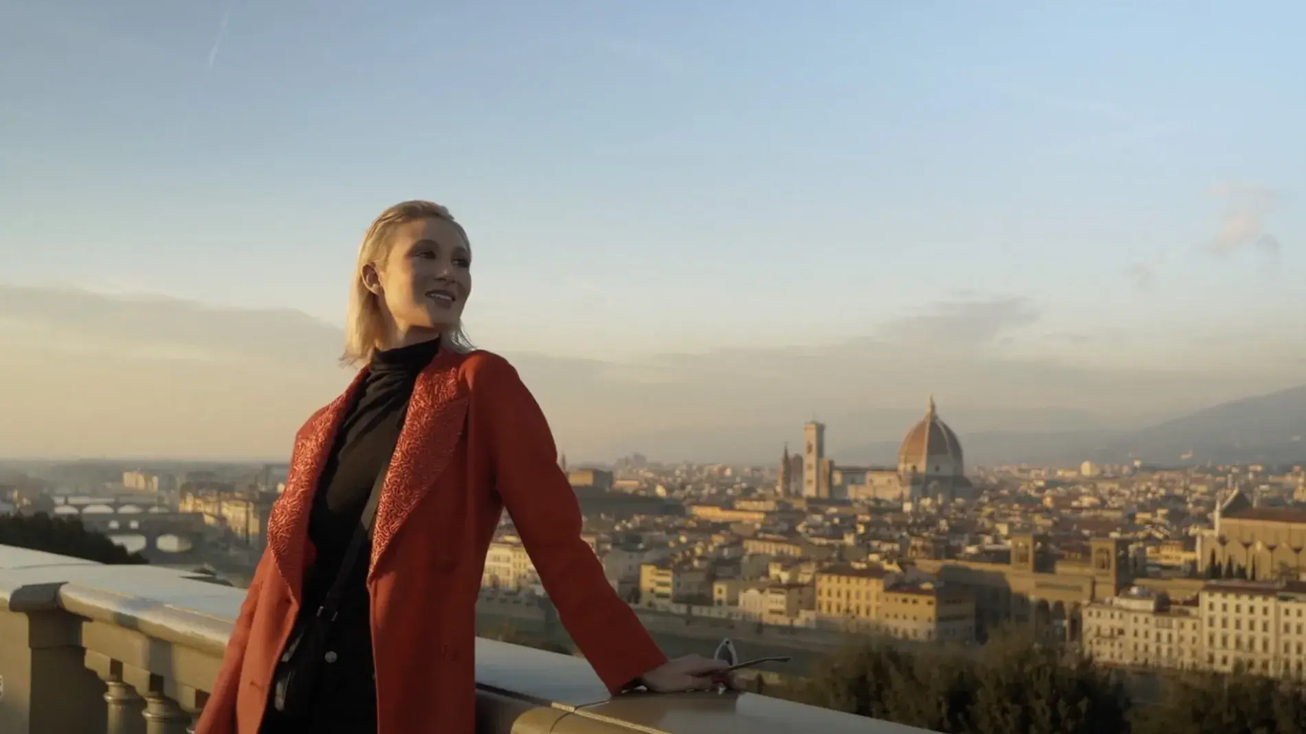 Film still of "Va Bene Così" a comedy short film written and directed by Peter Allen Stone that was filmed in Florence, Italy, woman in red coat stands on a bridge over looking Florence.