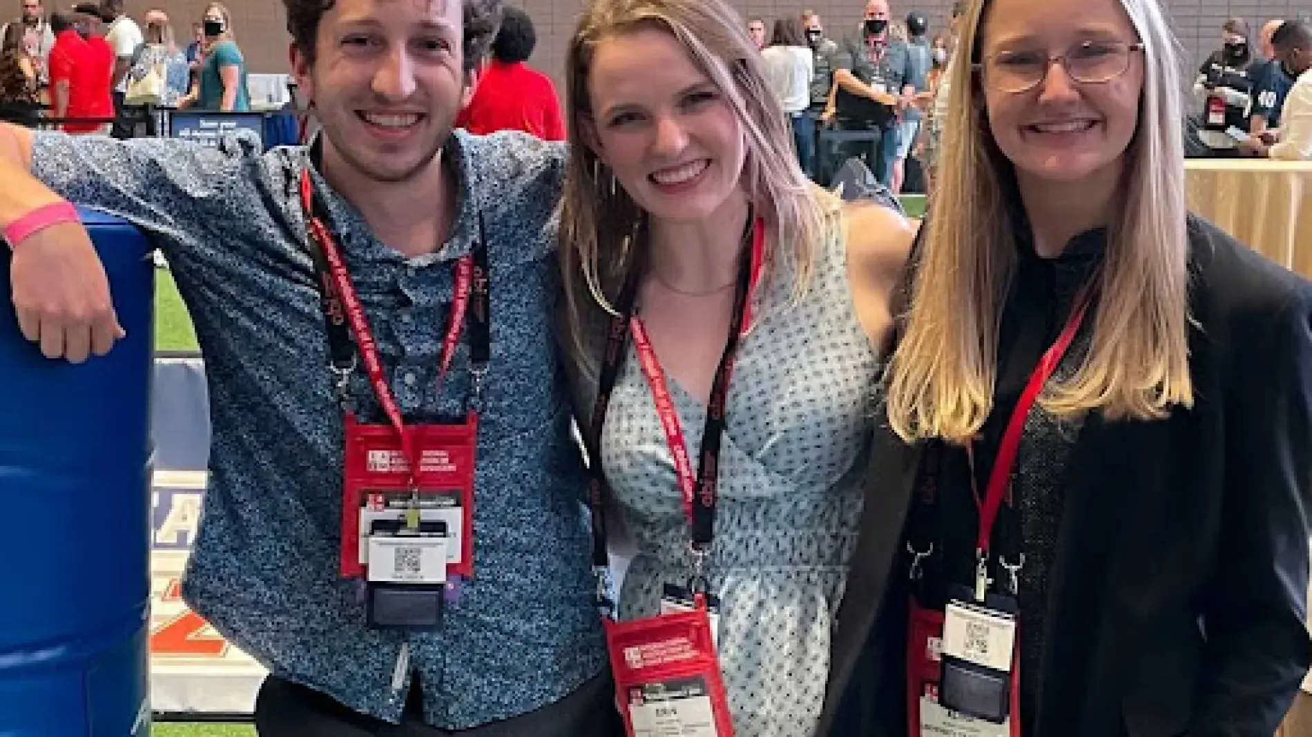 Three students pose together at a conference, wearing lanyards 