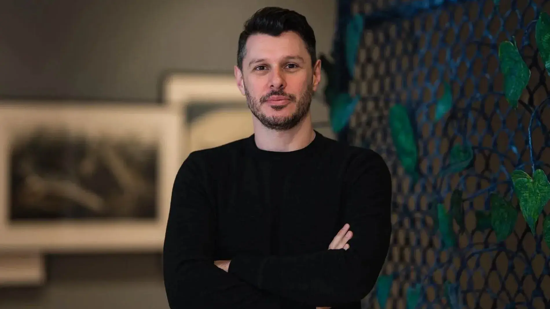 Headshot of Aaron Garvey in art gallery wearing a dark shirt, with art in the background