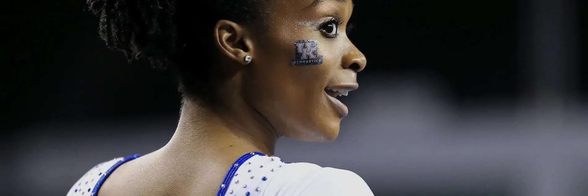 Image of UK student athlete in gymnastics leotard and the UK lockup in facepaint on her cheek