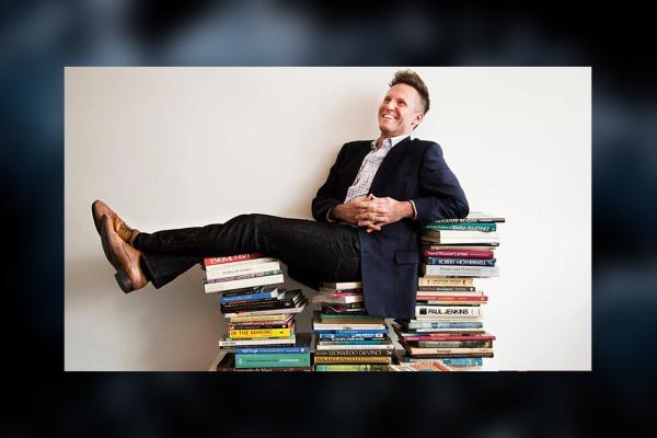 Image of Theo Edmonds wearing a dark suit sitting on a stack of books
