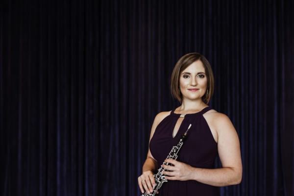 Image of Dr. ToniMarie Marchioni holding oboe, wearing black dress, against black curtain backdrop