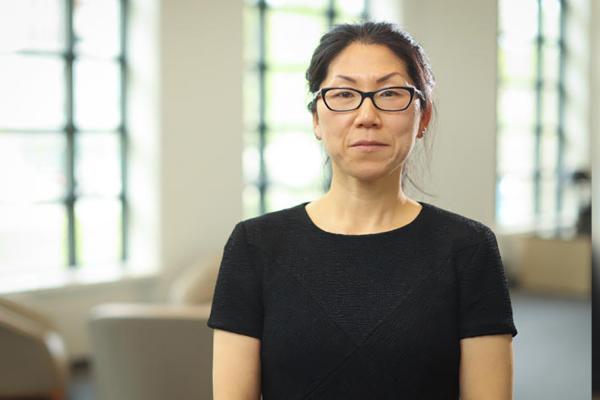 Image of Yuha Jung seated in front of bright windows wearing a black shirt and black glasses