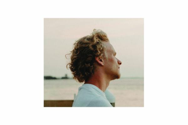 Image of Dylan Shade in profile with a body of water behind him, wearing a light blue shirt