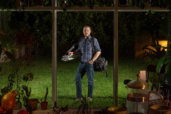 Image of Rob Southard standing outside of window, with his camera around his shoulder at night