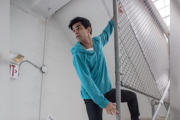 Image of Taha Mandviwala in a teal hoodie climbing a chain link fence