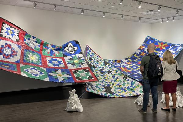 Patrons view an art installation of large patchwork quilts.