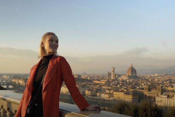 Film still of "Va Bene Così" a comedy short film written and directed by Peter Allen Stone that was filmed in Florence, Italy, woman in red coat stands on a bridge over looking Florence.