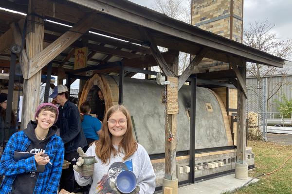 Students hold up finished ceramic pieces outside of new kiln
