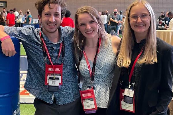 Three students pose together at a conference, wearing lanyards 
