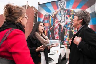 three people talking in front of outdoor mural