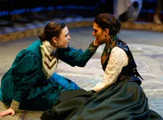 two women in period costumes looking at each other on stage floor