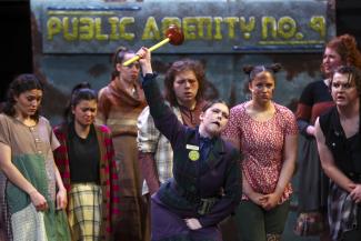 People on stage with woman in center holding plunger above head