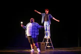 two actors on stage one on ladder