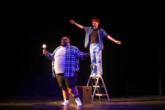 two actors on stage one on ladder