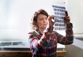 A student holding a transparent sheet of negatives up to the light with a small magnifying glass.