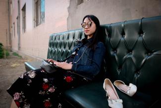 A woman sitting on a tufted dark green leather couch outside in an alley.