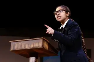 person on stage at podium pointing outward
