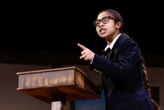 person on stage at podium pointing outward