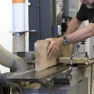 A student pushes a rough sawn board through a jointer to flatten the sides.