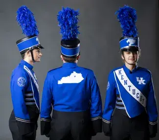 three students in blue band uniforms for the university of kentucky on a gray background