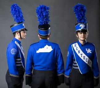 three students in blue band uniforms for the university of kentucky on a gray background