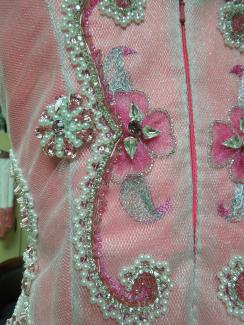 Pearls, seafom beads, and faux gems adorn a sheer metallic fabric layered over the vibrant pink bodice of a dress on a manequin.