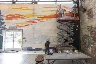 Greyline station mural student on lift painting on tall wall