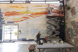 Greyline station mural student on lift painting on tall wall