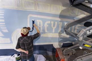 student painting word greyline on greyline station mural