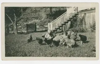 black and white photo of child surrounded by chickens