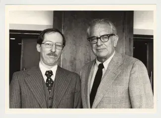 Yellowed black and white photo. A gently smiling Richard Domek (right) sports a mustache and pinstripe suit next to form university president Otis A. Singletary (right) with black rimmed glasses and a light tweed suit.