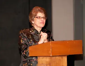 Geri Maschio looking outward with hands clasped standing at podium