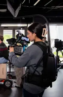 AA student with a full camera and backpack rig records a workshop in the Cornerstone meeting space.