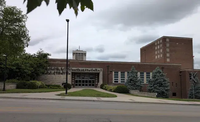 A current photo of the Fine Arts Building from the opposite side of Rose Street. Many more trees have grown up around the building but the doors, walkways, and drumstick-shaped patch of front lawn have remained the same.
