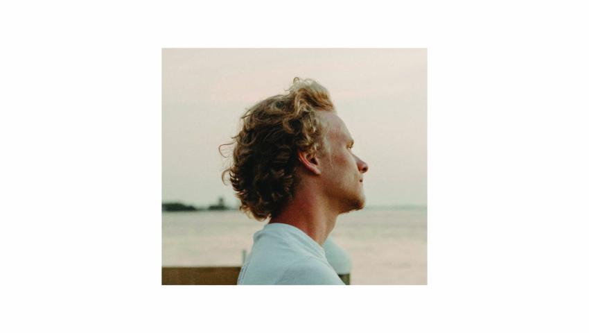 Image of Dylan Shade in profile with a body of water behind him, wearing a light blue shirt