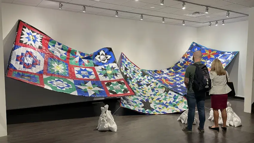 Patrons view an art installation of large patchwork quilts.