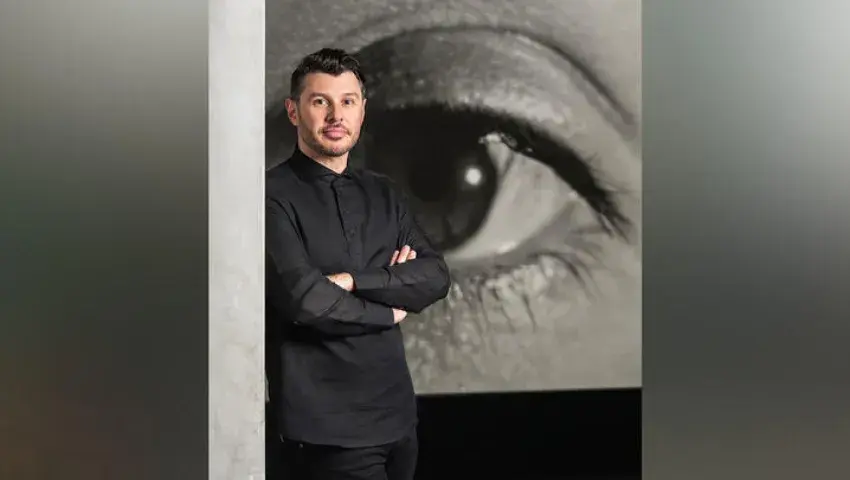 Image of Aaron Levi Garvey wearing a black shirt with his arms folded in front of a large sketch of an eye