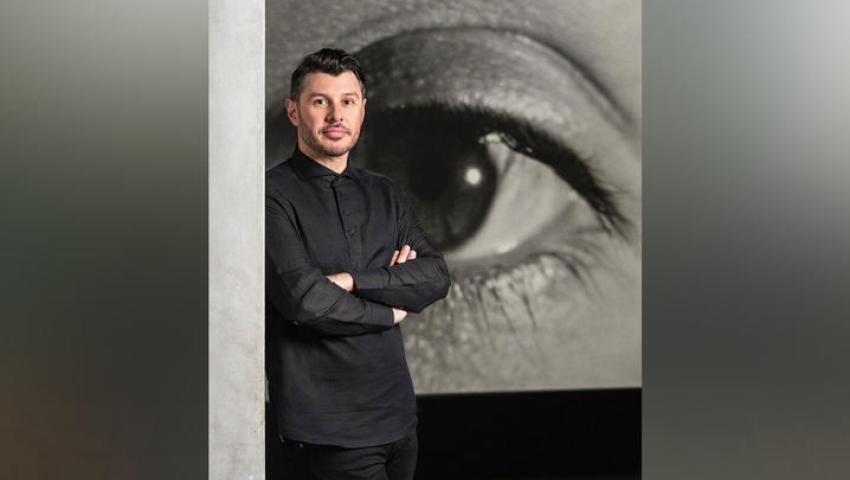 Image of Aaron Levi Garvey wearing a black shirt with his arms folded in front of a large sketch of an eye