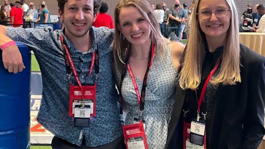 Three students pose together at a conference, wearing lanyards